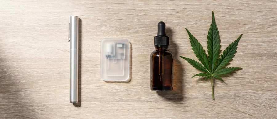 Einweg-Vape oder Pod-System: Stift, Kartusche und Fläschchen nebeneinander auf hellem Holz mit Hanfblatt